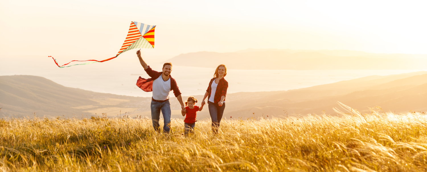 Happy family running through meadows in sunset, knowing they have the relevant protection in place